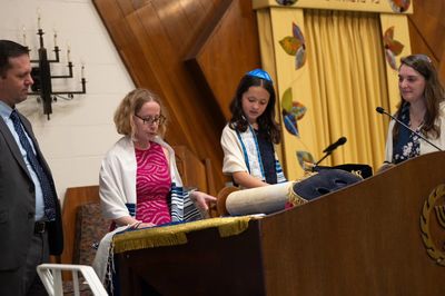 A bat mitzvah girl gets ready to read Torah while her parents bless and Rabbi Noyo looks on.