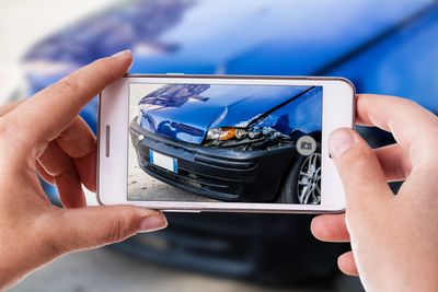 person taking a photo with a smart phone of a blue crashed car