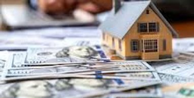 A miniature house model on stacks of US dollar bills with a blurred person in the background.
