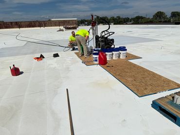 Two workers in neon shirts working on a large white rooftop with equipment and supplies.