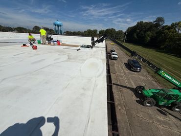 Workers on a large white rooftop with machinery and vehicles below.