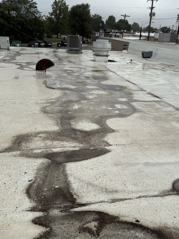Flat rooftop with ventilation units and water stains under a cloudy sky.