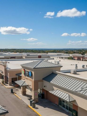 A shopping plaza under a clear blue sky with scattered clouds.