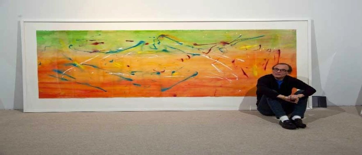 Man sits by large abstract painting with orange, green.