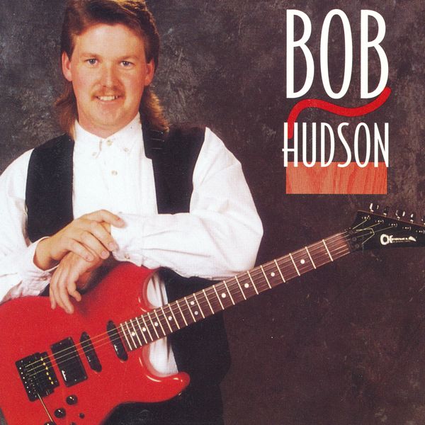 Bob Hudson posing with a red electric guitar against a dark backdrop.