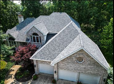 A large brick house with a multi-gabled roof surrounded by greenery.