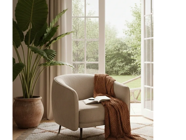 Cozy beige armchair with a brown knitted throw and open book near a large plant and open glass door.