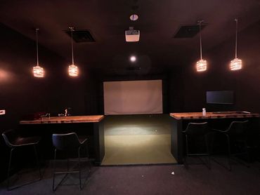 Dark room with bar stools, pendant lights, and a projector screen.