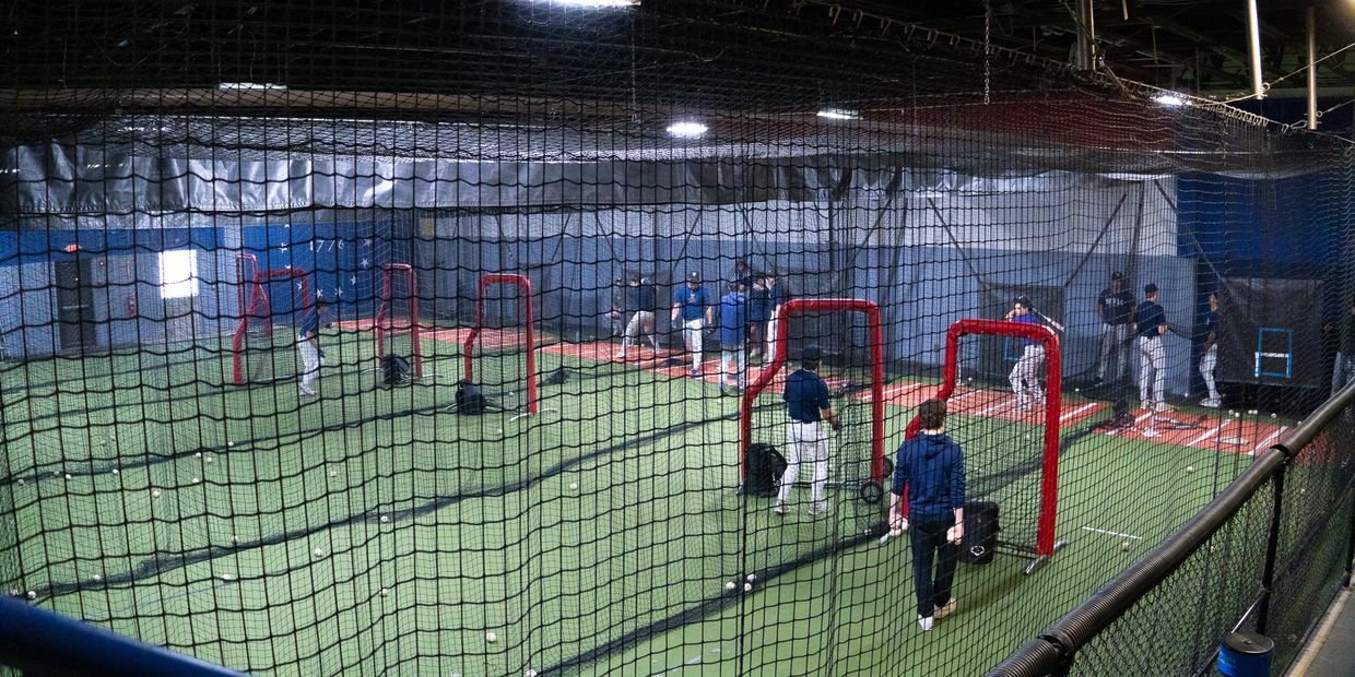 Indoor baseball practice with multiple players hitting and pitching.