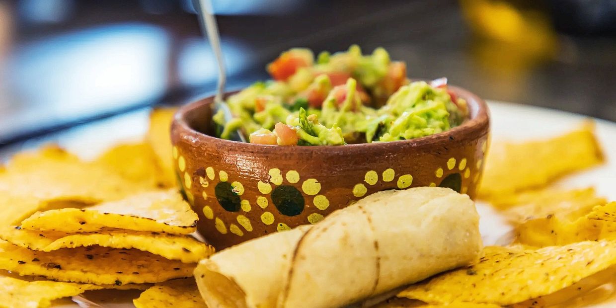 A colorful bowl of guacamole, garnished with diced tomatoes, is surrounded by crispy tortilla chips