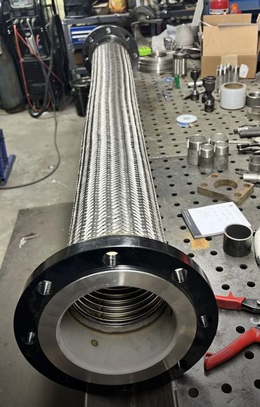 A large industrial metal hose with a braided exterior on a workshop table.