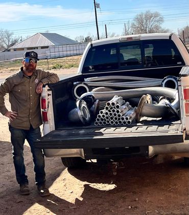 Man standing next to pickup truck loaded with metal hose and fittings.