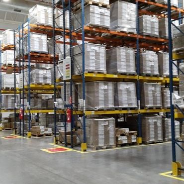 Warehouse shelves stacked with palletized goods wrapped in plastic.