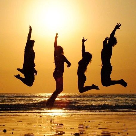 Image of four people jumping on beach at sunset