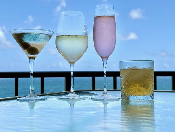 Four beverage glasses on outside table with sky in background showing condensation