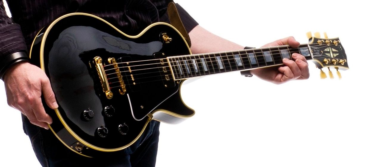 Person playing a black electric guitar with gold hardware.