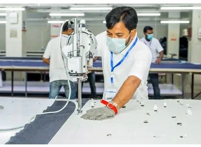 A man wearing a mask operates a fabric cutting machine in a factory.