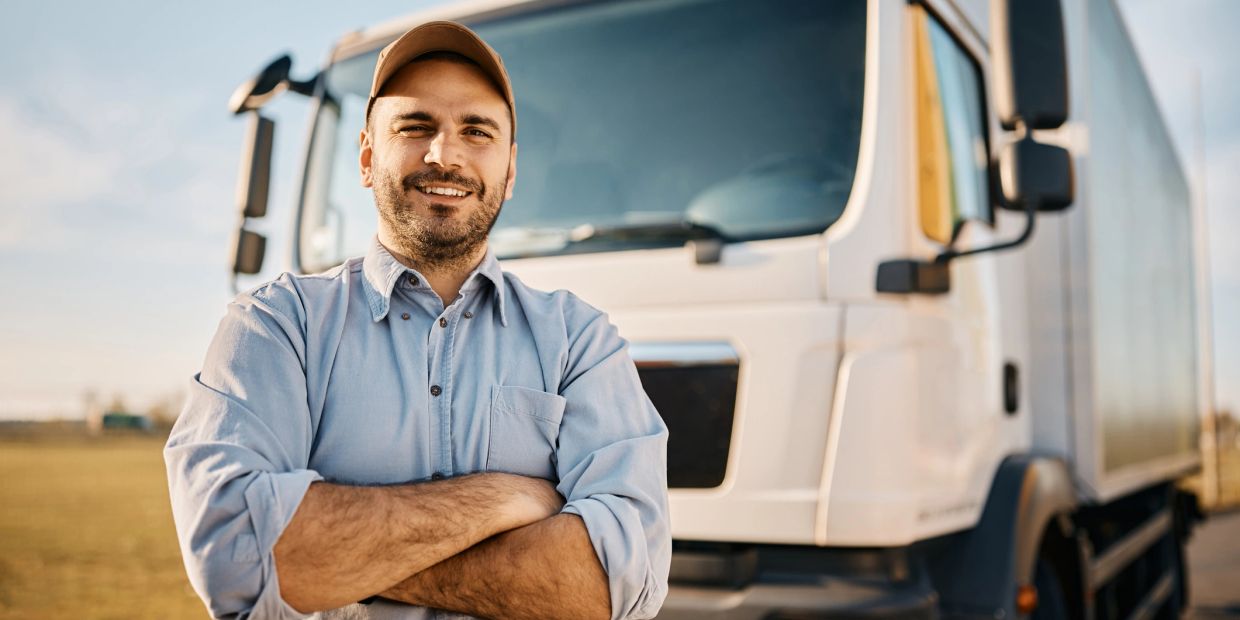 Confident truck driver standing with arms crossed in front of a truck.