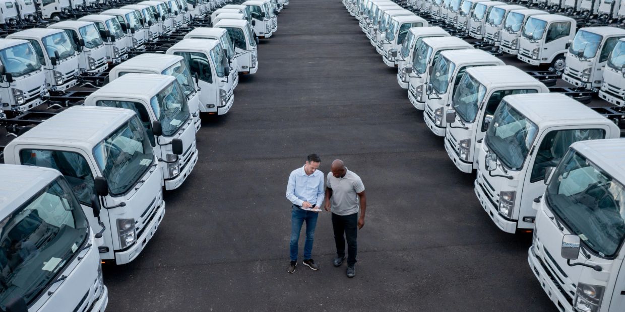 Two men standing between rows of white trucks.