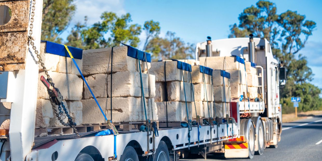 Truck transporting large stone blocks on highway.