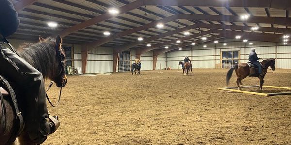 Riders on horses inside a large, well-lit indoor arena.