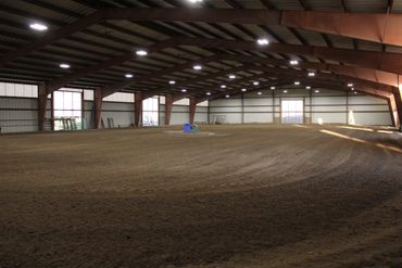Large indoor arena with dirt floor and overhead lights.
