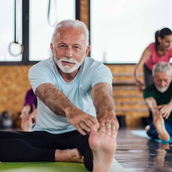Hombre mayor haciendo estiramientos en clase de yoga.