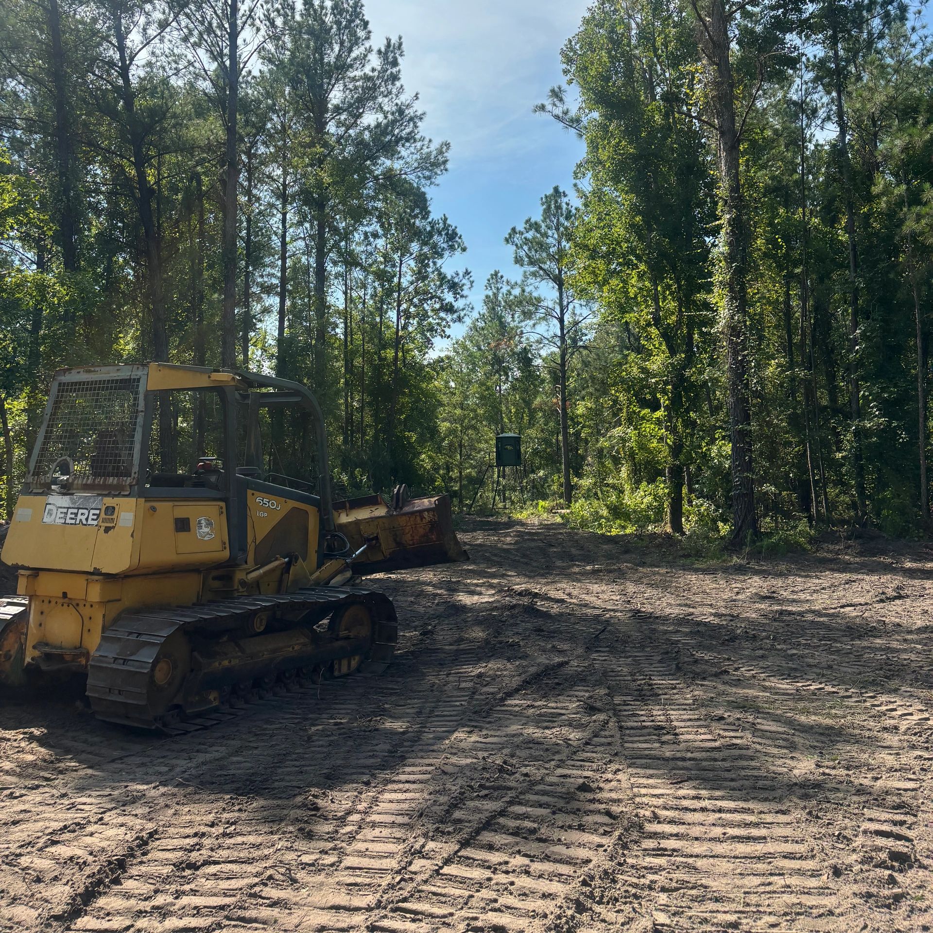 John Deere bulldozer in a forest clearing with a deer blind in the distance.