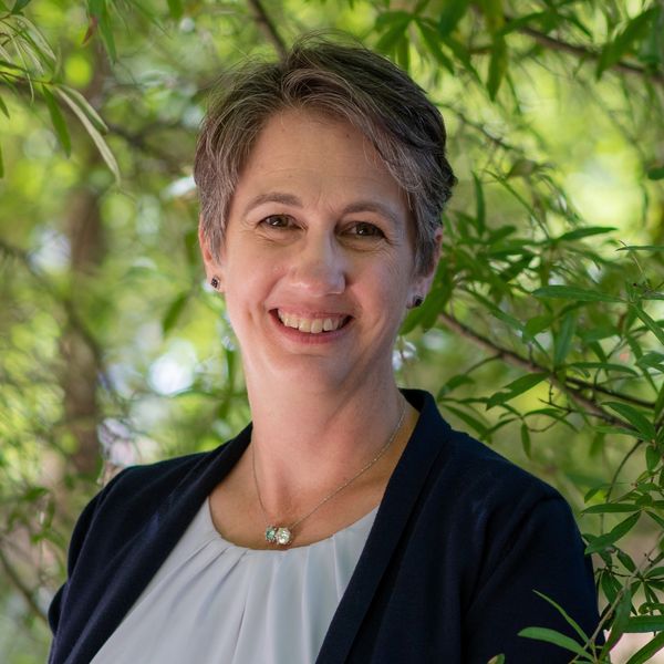 Robyn Jordan, MD wearing a navy blazer and white blouse, standing outdoors in front of trees
