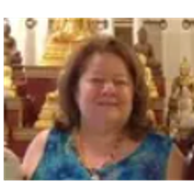 Woman in a blue top smiling indoors with decorative background.