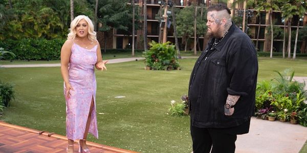 A woman in a pink dress and a man in black standing outdoors.