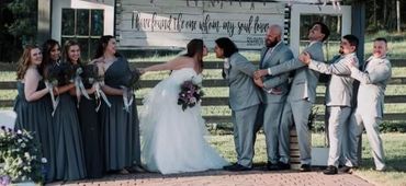 A couple kissing before their marriage as their wedding party pulls them apart.