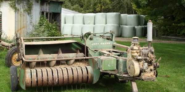  John Deere model 14T square baler with wrapped high moisture round bales in background