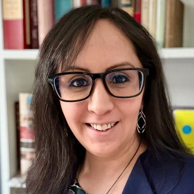 Smiling woman with glasses in front of a bookshelf.