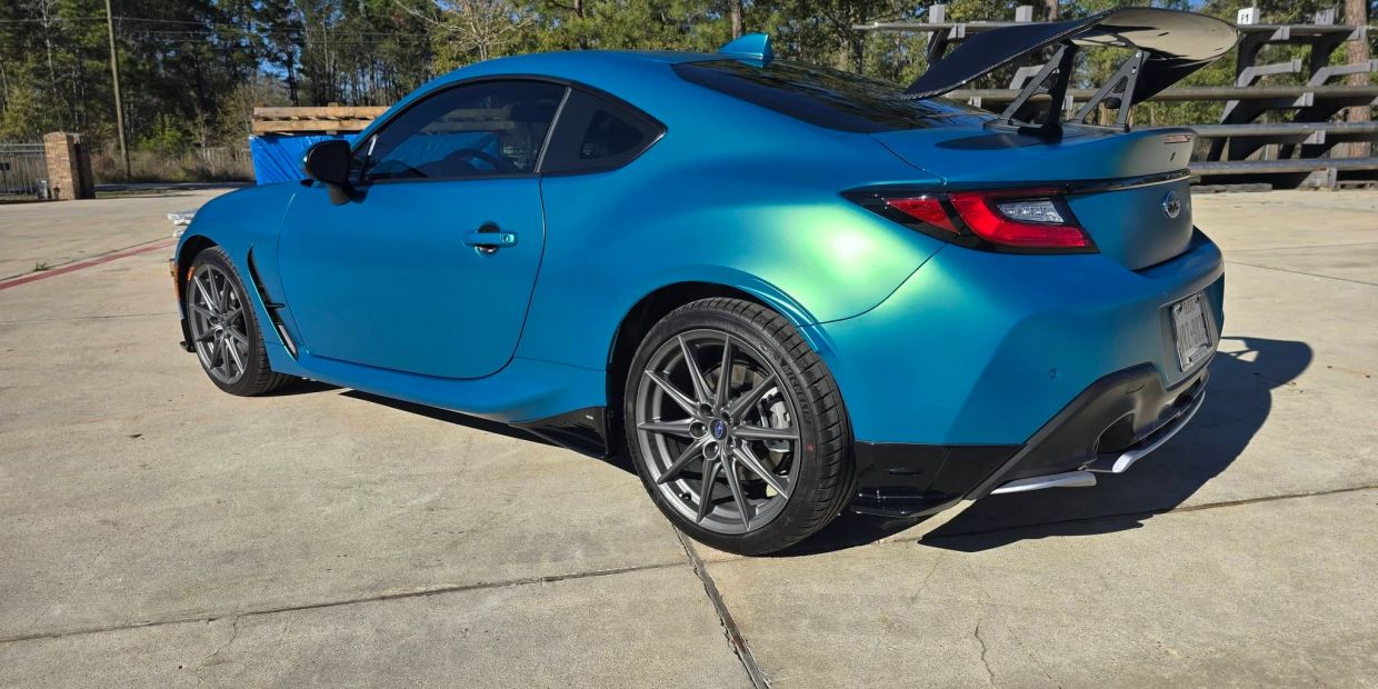 Blue sports car with large rear wing parked outdoors.