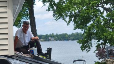 Man sitting on a roof by a lake.
