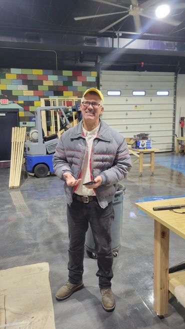 Man in workshop holding a phone, smiling.
