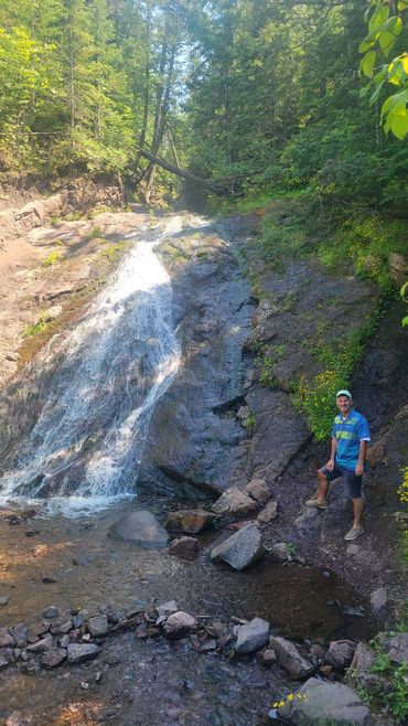 Man standing by a small waterfall in a forest.