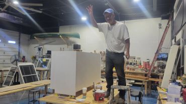 Man gesturing inside a workshop with woodworking tools.