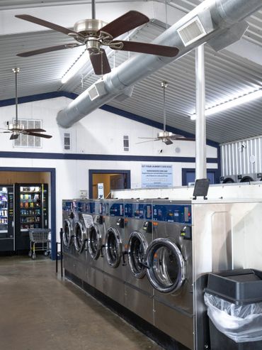Interior of a clean laundromat with washing machines and ceiling fans.