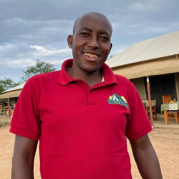 Luxury Safari Camp Housekeeping Manager Smiling with luxury tent in background