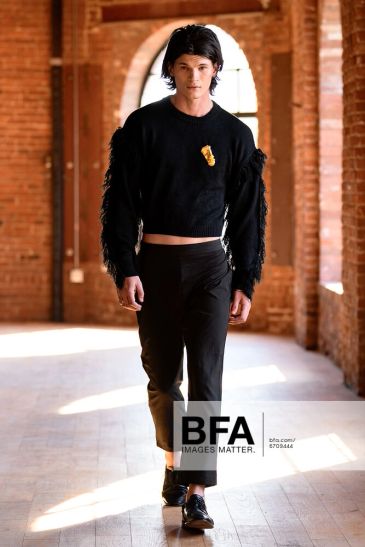 Male model walking down a brick corridor in all black outfit.