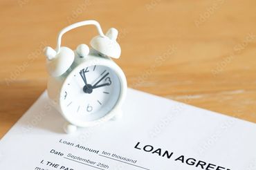 A white alarm clock on top of a loan agreement document on a wooden table.