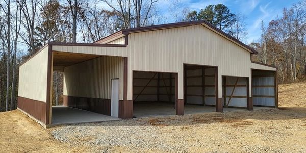 A large metal barn with multiple open bays and a side door in a wooded area.