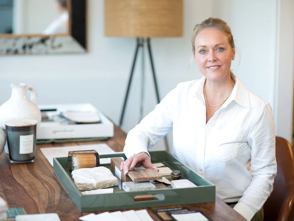 A woman in white shirt showing material samples on a wooden table.