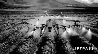 Agricultural drones spraying crops in a vast field with mountains in the background.