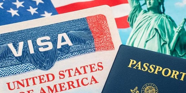 A close-up of a U.S. visa and a passport with the American flag and Statue of Liberty in the background.