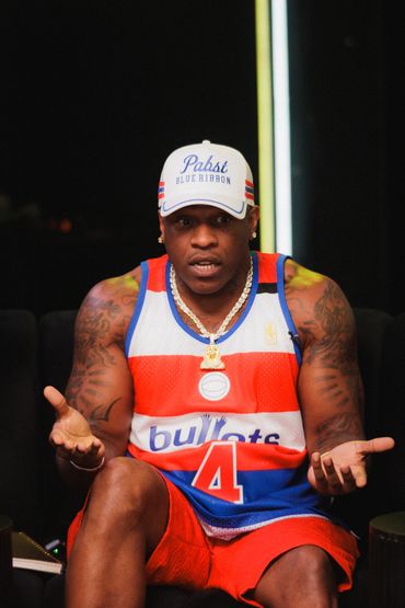 Man in a basketball jersey and cap gesturing with hands.