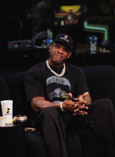 A man in a black Lakers T-shirt and cap sits relaxed on a couch.