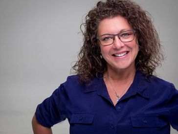 Lynn Nichols wearing a blue shirt in front of a gray background.